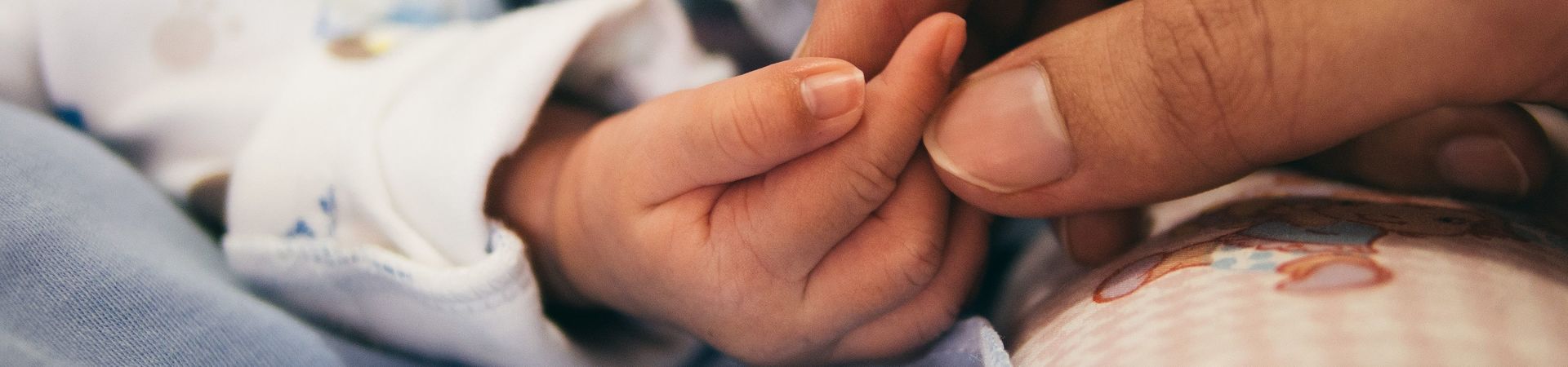 Person hält die Hand eines Neugeborenen