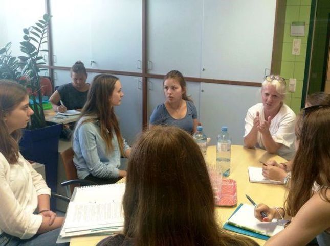Ärztin sitzt mit Schülerinnen an einem Tisch und erklärt ihnen etwas