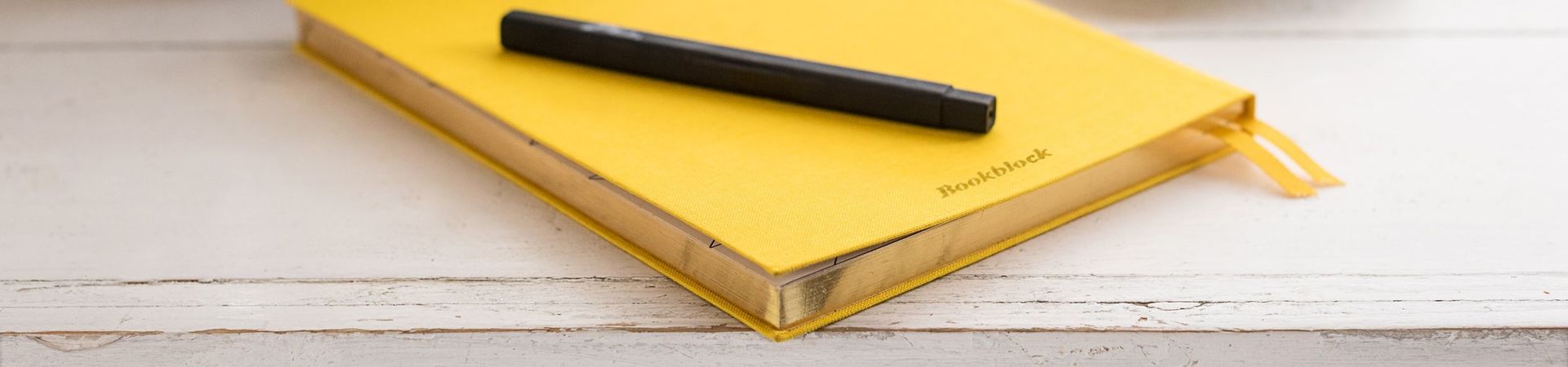 Gelbes Notizbuch und schwarzer Stift liegen auf einem Holztisch