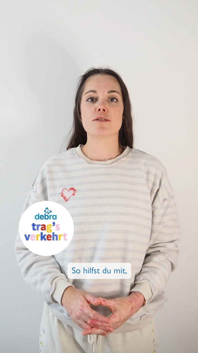 Eine junge Frau mit EB trägt einen Pulli verkehrtherum und schaut in die Kamera