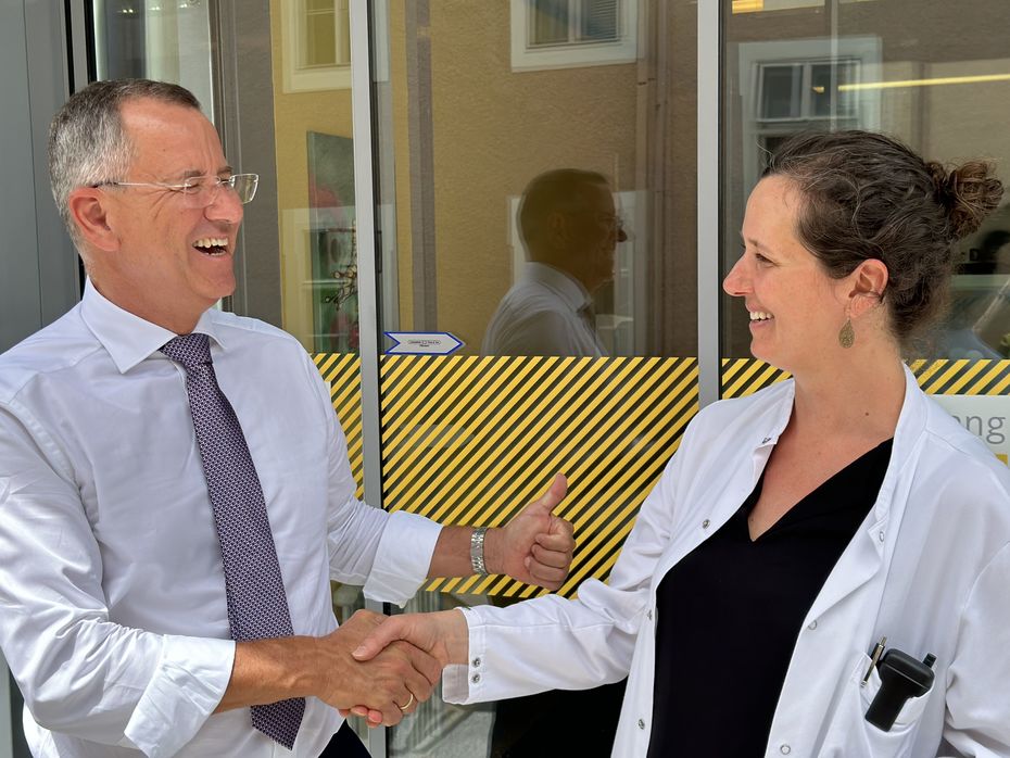 Ein Mann und eine Frau geben sich die Hand. Im Hintergrund der Eingang eines Gebäudes.