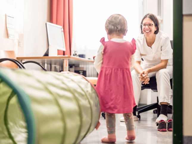 Freundlich lächelnde Ärztin wartet auf Kind in Behandlungszimmer