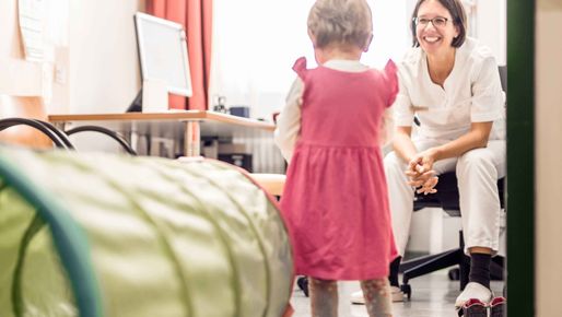 Freundlich lächelnde Ärztin wartet auf Kind in Behandlungszimmer