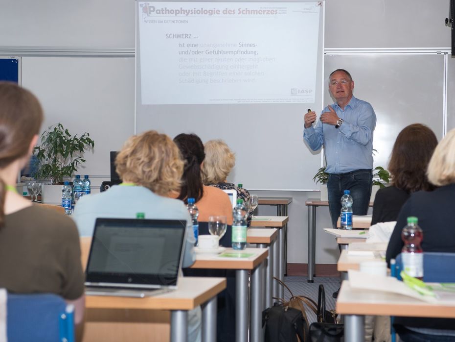 Vortragender im Hintergrund, TeilnehmerInnen des Symposiums im Vordergrund sitzend