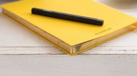 Schwarzer Stift auf gelbem Notizbuch auf einem Holztisch