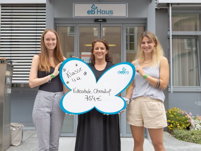 Drei junge Frauen bei der Übergabe eines Spendenschecks vor dem EB-Haus Austria 